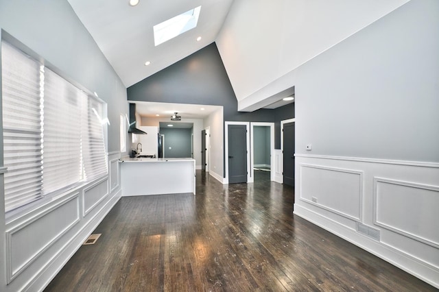 unfurnished living room with a skylight, dark wood finished floors, a wainscoted wall, a decorative wall, and a sink