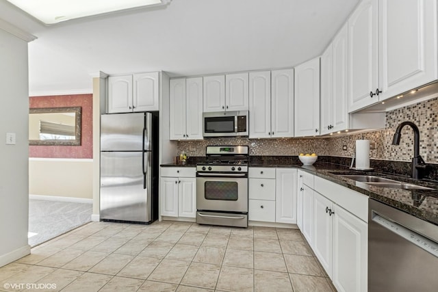 kitchen featuring decorative backsplash, dark stone countertops, stainless steel appliances, white cabinetry, and a sink