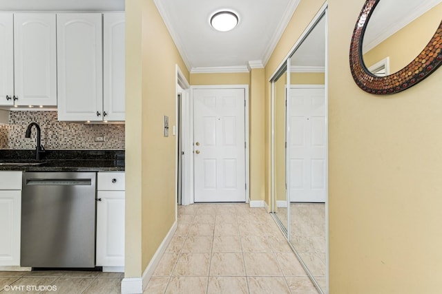 kitchen featuring ornamental molding, dark stone countertops, stainless steel dishwasher, white cabinetry, and a sink