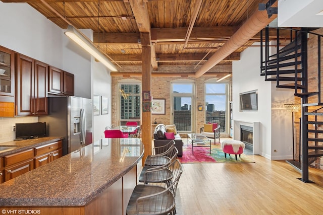 kitchen with stainless steel fridge with ice dispenser, wood ceiling, light wood-style flooring, open floor plan, and a lit fireplace