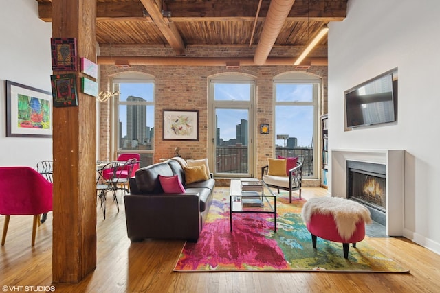 living room featuring brick wall, beamed ceiling, a lit fireplace, and hardwood / wood-style floors