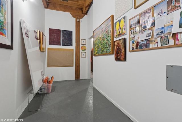 corridor with concrete flooring, beam ceiling, and baseboards