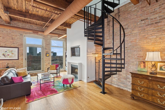 living room with a fireplace, stairway, brick wall, wood finished floors, and beamed ceiling