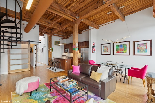 living area with a barn door, a towering ceiling, wood ceiling, light wood-type flooring, and beam ceiling