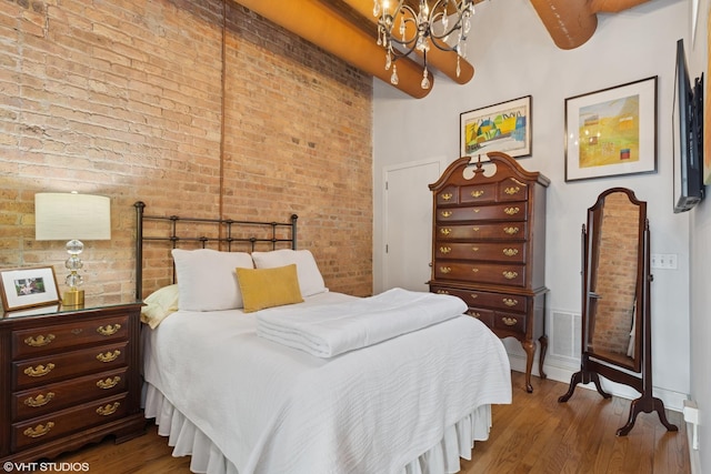 bedroom featuring brick wall, wood finished floors, and an inviting chandelier