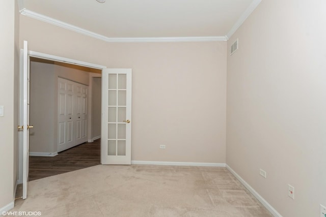 carpeted empty room with visible vents, french doors, baseboards, and ornamental molding