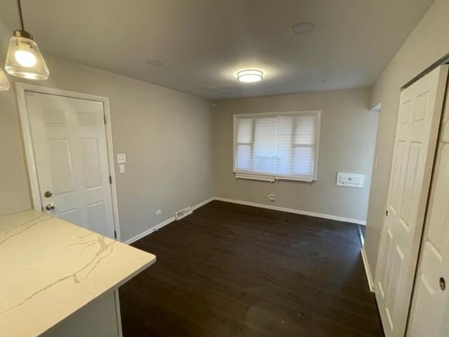 unfurnished dining area featuring dark wood-style flooring, visible vents, and baseboards