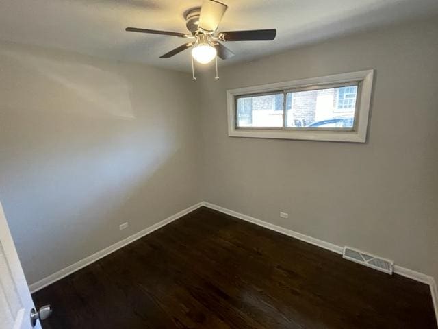 empty room with ceiling fan, dark wood finished floors, visible vents, and baseboards