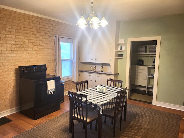 dining space featuring a notable chandelier, brick wall, wood finished floors, visible vents, and baseboards