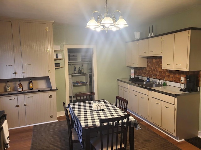 kitchen featuring decorative backsplash, dark wood-type flooring, a sink, pendant lighting, and a notable chandelier