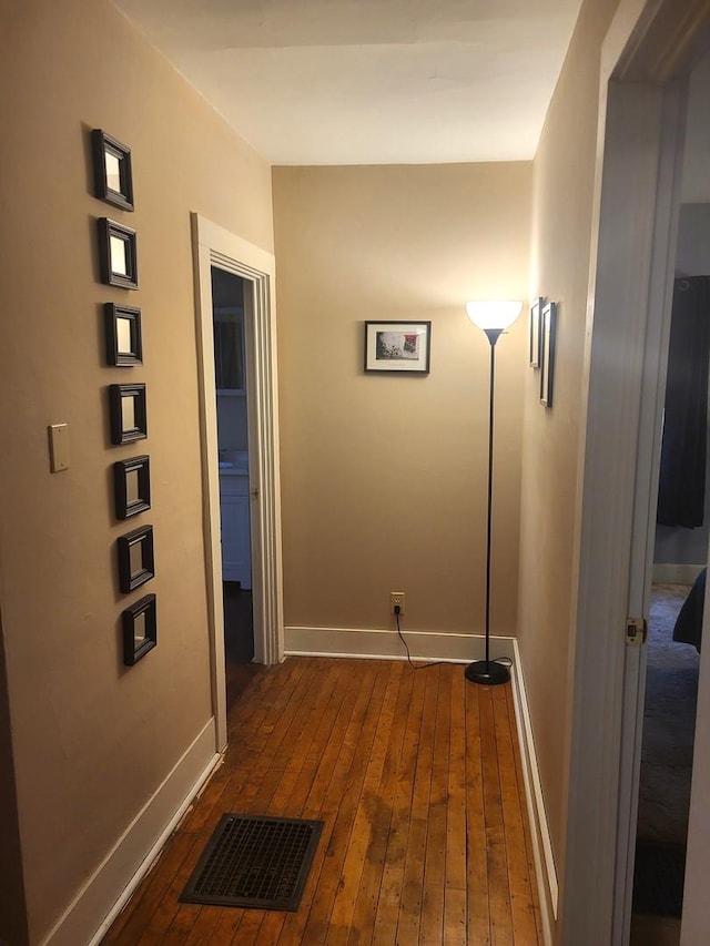 hall featuring dark wood-style floors, visible vents, and baseboards