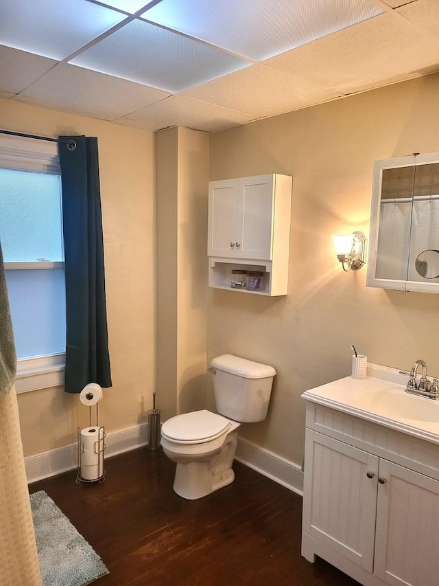 bathroom with a paneled ceiling, toilet, wood finished floors, vanity, and baseboards