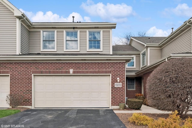 view of front of home featuring driveway, an attached garage, and brick siding