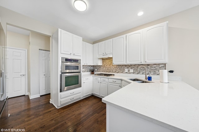 kitchen with stainless steel appliances, tasteful backsplash, white cabinetry, a sink, and a peninsula