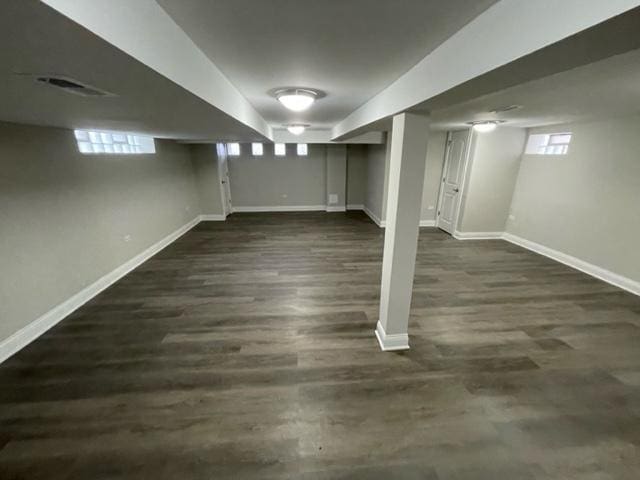 below grade area with dark wood finished floors, visible vents, and baseboards
