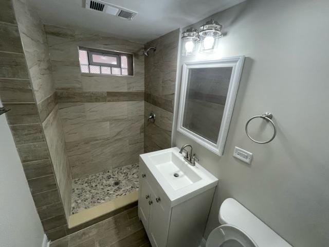 bathroom with visible vents, vanity, toilet, and tiled shower