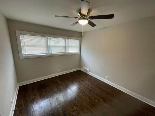 spare room with dark wood-type flooring, visible vents, and baseboards