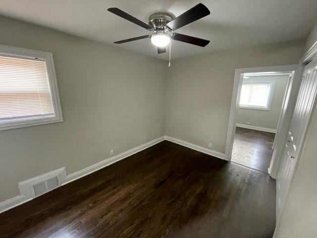 unfurnished room with baseboards, visible vents, dark wood finished floors, and a ceiling fan