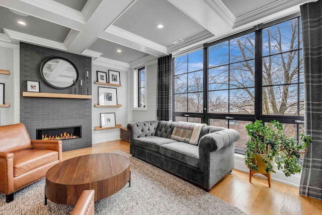 living area featuring beam ceiling, crown molding, a brick fireplace, wood finished floors, and coffered ceiling