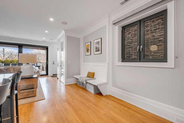 interior space featuring a decorative wall, recessed lighting, baseboards, light wood-style floors, and crown molding