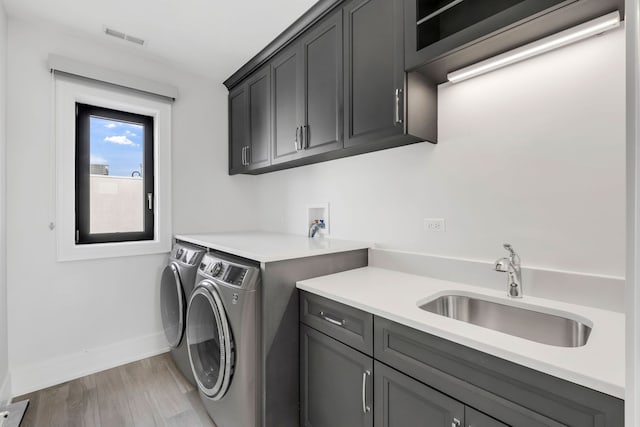 laundry area featuring light wood finished floors, cabinet space, visible vents, washing machine and dryer, and a sink