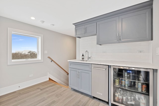 bar featuring wine cooler, tasteful backsplash, a sink, light wood-type flooring, and baseboards