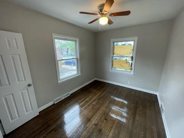 empty room featuring visible vents, dark wood finished floors, baseboards, and ceiling fan