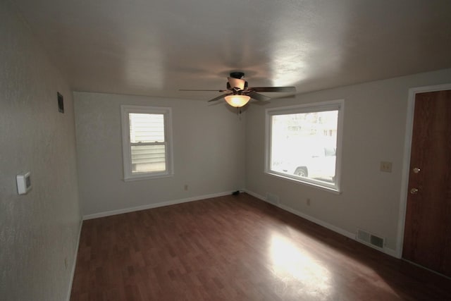 unfurnished room featuring a healthy amount of sunlight, baseboards, visible vents, and dark wood-style flooring