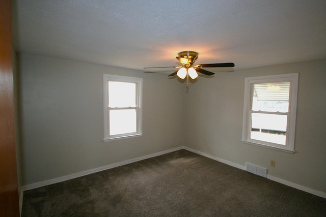 empty room with baseboards, visible vents, dark carpet, and a wealth of natural light