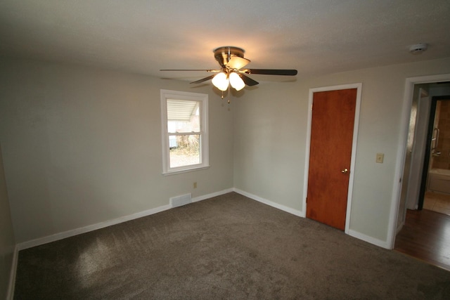 empty room with ceiling fan, dark carpet, visible vents, and baseboards