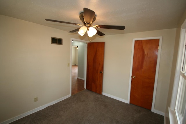 unfurnished bedroom with a textured ceiling, a ceiling fan, visible vents, baseboards, and dark colored carpet