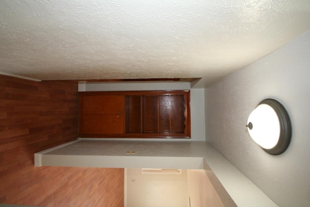 hall featuring wood walls, light wood finished floors, and a textured ceiling