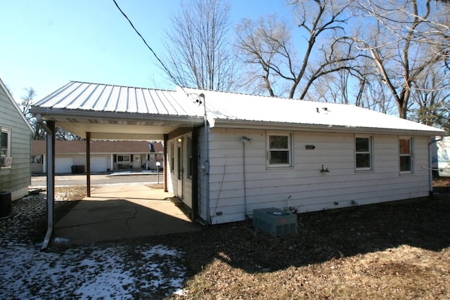 back of property featuring driveway, a carport, metal roof, and central AC