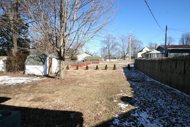 snowy yard featuring a storage shed, an outdoor structure, and fence