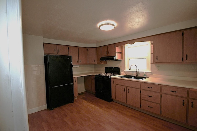 kitchen with under cabinet range hood, a sink, light wood-style floors, light countertops, and black appliances