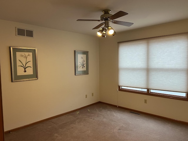 carpeted empty room featuring visible vents, a ceiling fan, and baseboards