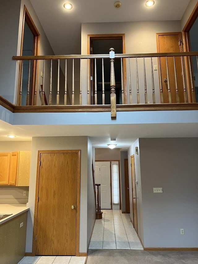 stairway with tile patterned floors, carpet flooring, baseboards, and a towering ceiling