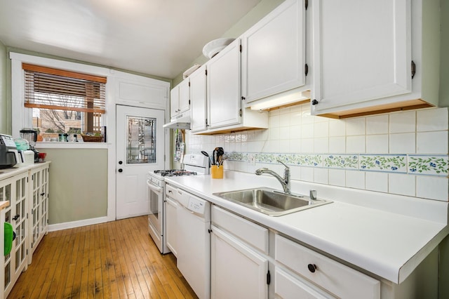 kitchen with white appliances, backsplash, a sink, and white cabinets