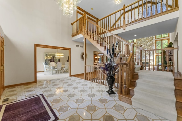 staircase with a chandelier, visible vents, a towering ceiling, and baseboards