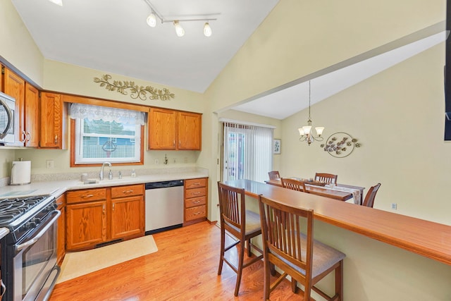 kitchen featuring light wood-style flooring, stainless steel appliances, a sink, vaulted ceiling, and light countertops