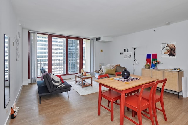 dining area featuring a wall of windows, wood finished floors, visible vents, and baseboards