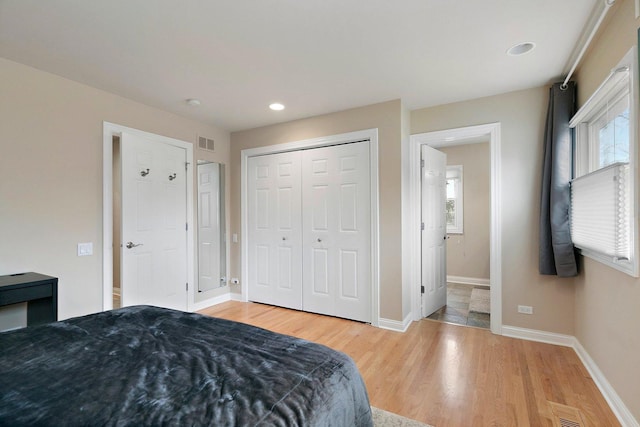 bedroom with a closet, wood finished floors, visible vents, and baseboards