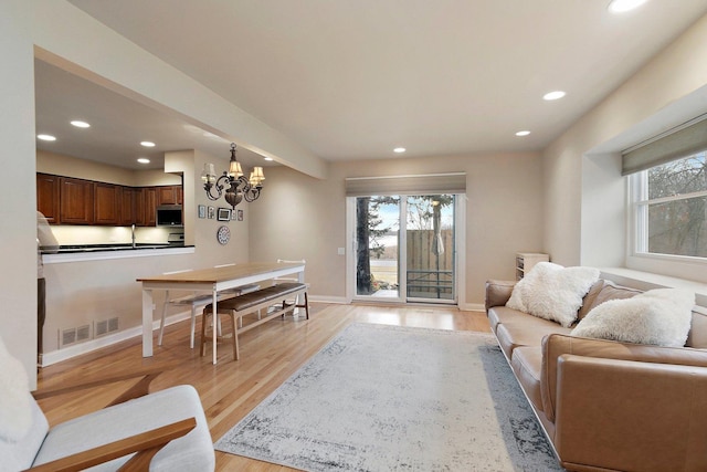 living area featuring light wood finished floors, baseboards, visible vents, a notable chandelier, and recessed lighting