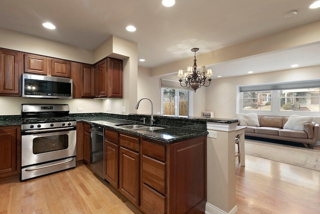 kitchen with light wood-style flooring, appliances with stainless steel finishes, a sink, dark stone countertops, and a peninsula