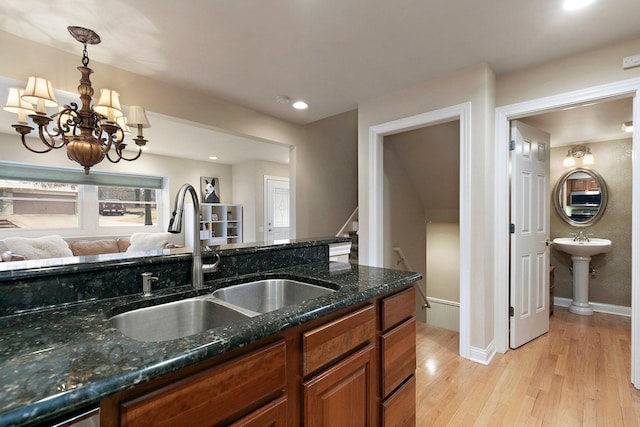 kitchen with dark stone counters, brown cabinetry, light wood-style floors, pendant lighting, and a sink