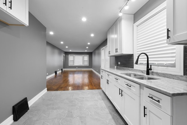 kitchen featuring visible vents, decorative backsplash, light stone counters, white cabinetry, and a sink