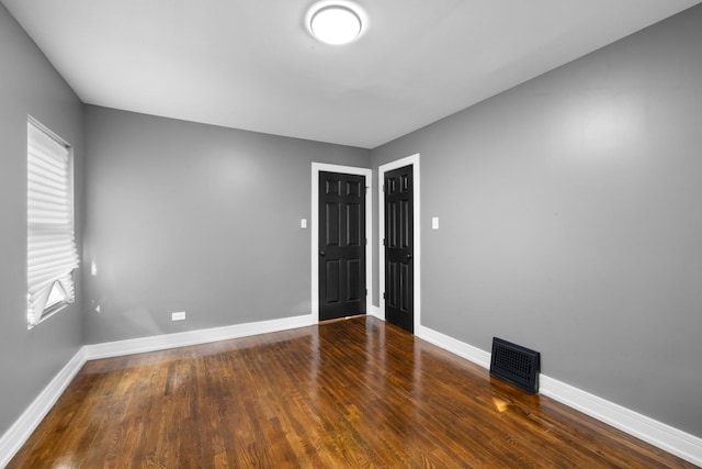 spare room featuring dark wood finished floors, visible vents, and baseboards