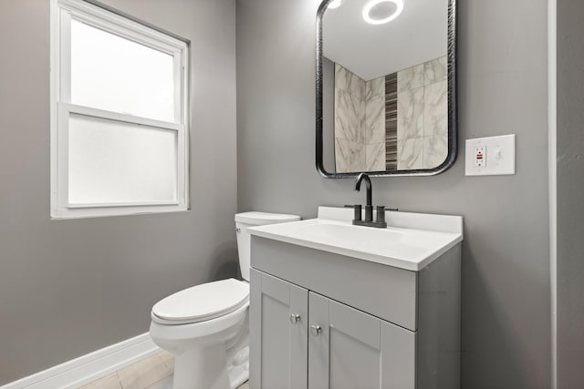 bathroom with toilet, plenty of natural light, vanity, and baseboards