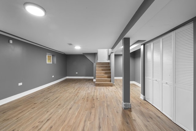 finished basement with light wood-style floors, visible vents, baseboards, and stairs