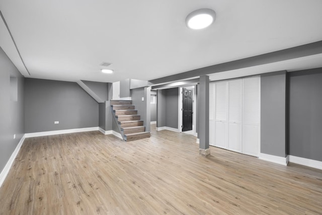 finished below grade area featuring light wood-type flooring, stairway, and baseboards